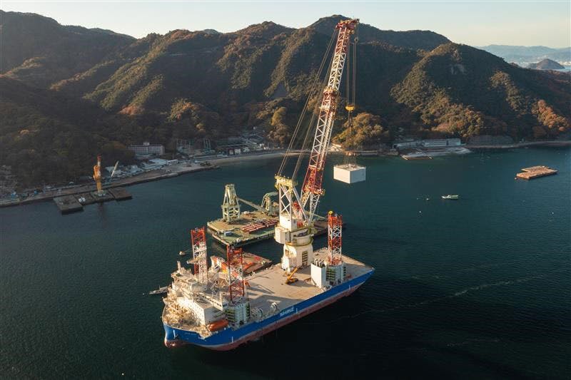 Aerial shot of a Blue Wind Shimizu Crane on the water, with mountain range in the background