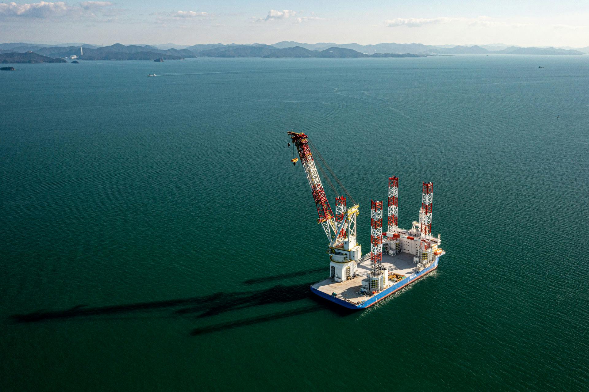 Wide shot of a Blue Wind Shimizu Telescopic leg crane offshore, with land and moutaintops in the background