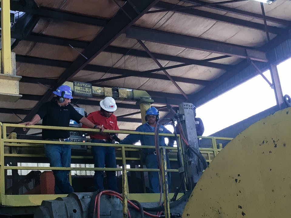 Michael Gaines interviewing two employees while looking over a handrail at machinery at the Grant Prideco facility in Navasota, TX
