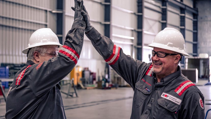 Two NOV employees wearing PPE, giving each other a high-five while inside a facility