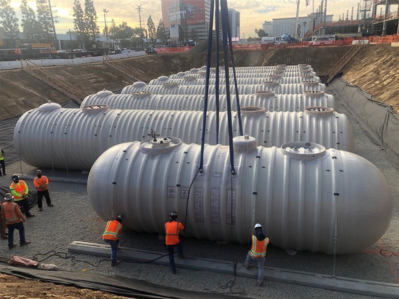 People installing a steel tank underground, with several more steel tanks already installed
