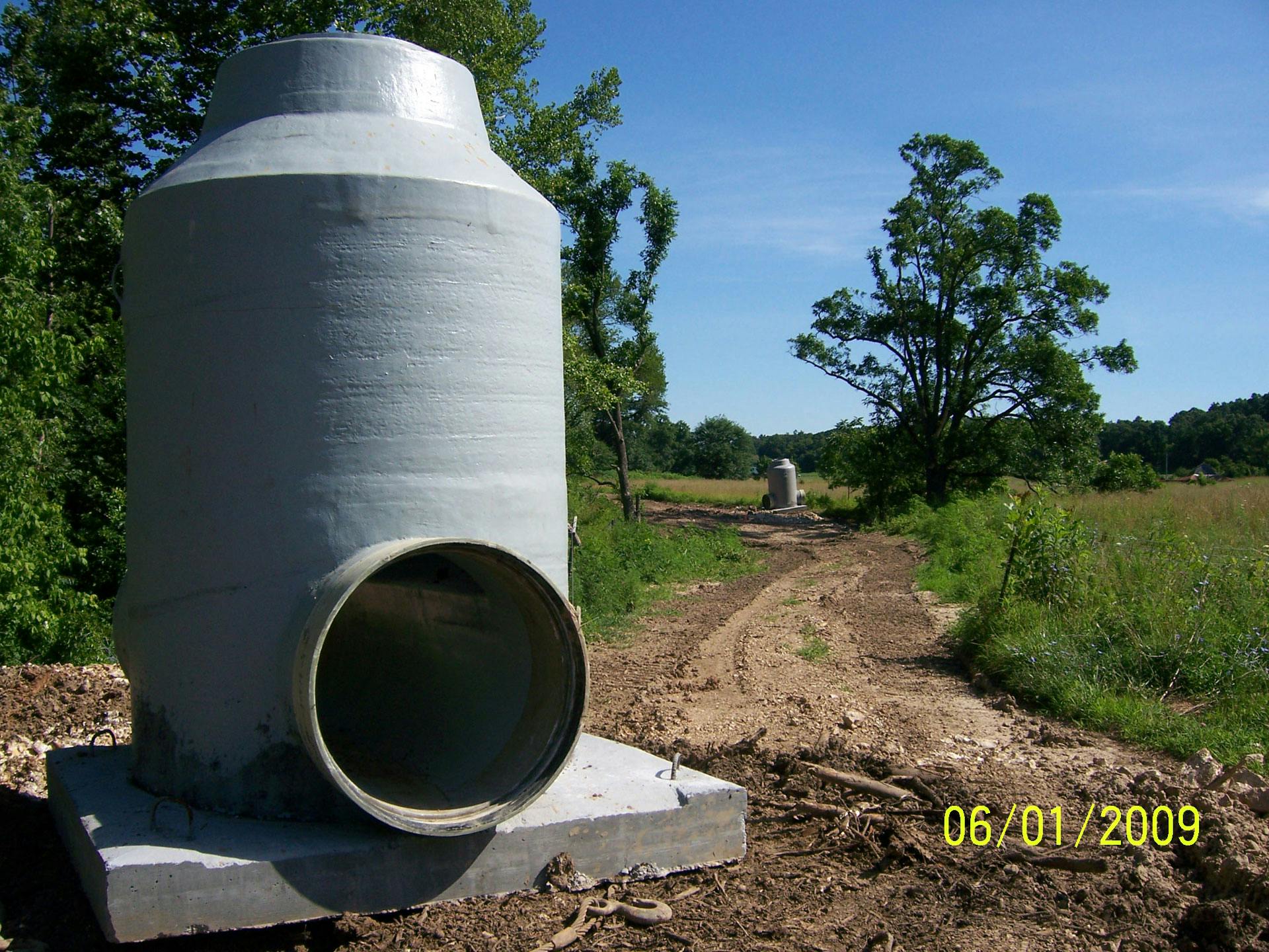 Individual FPR pipe on a concrete base, with trees in the background and a small FRP pipe in the distance
