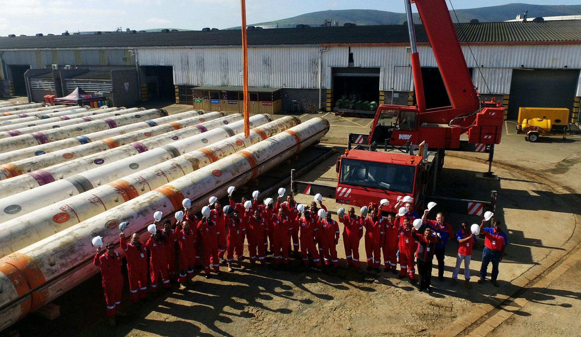 The NOV riser team at a facility with a red crane and tubing in the shot