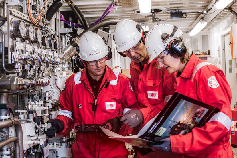 A group of rig trainers reference a guide while observing rig equipment