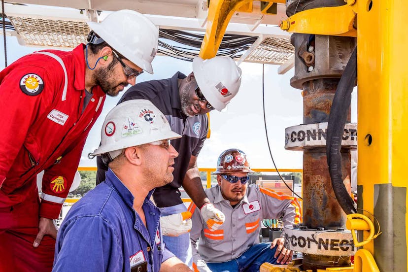 Four rig workers discuss tactics while examining a drill pipe connection on a rig
