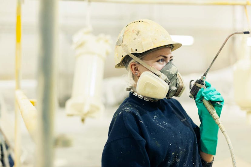 Technician with respirator mask sandblasting and/or painting