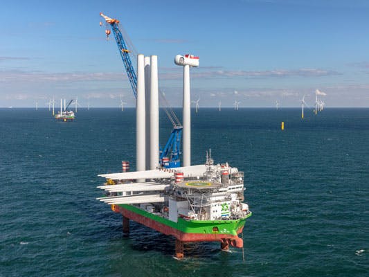 Wind turbine installation vessel with blue crane and wind turbines in the background