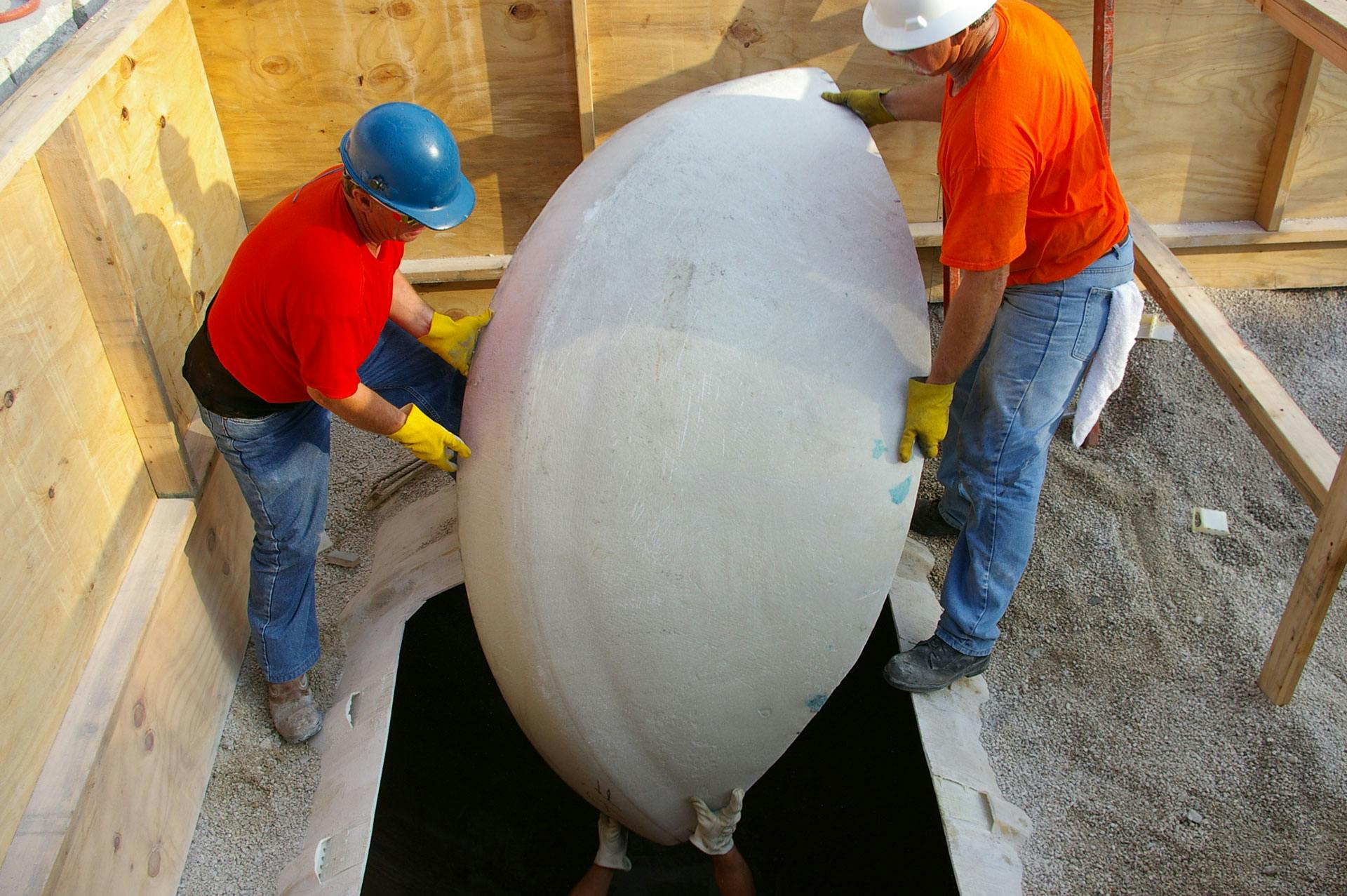 Two wokers lowering an end cap into and existing tank in the ground to a third worker inside the tank. 