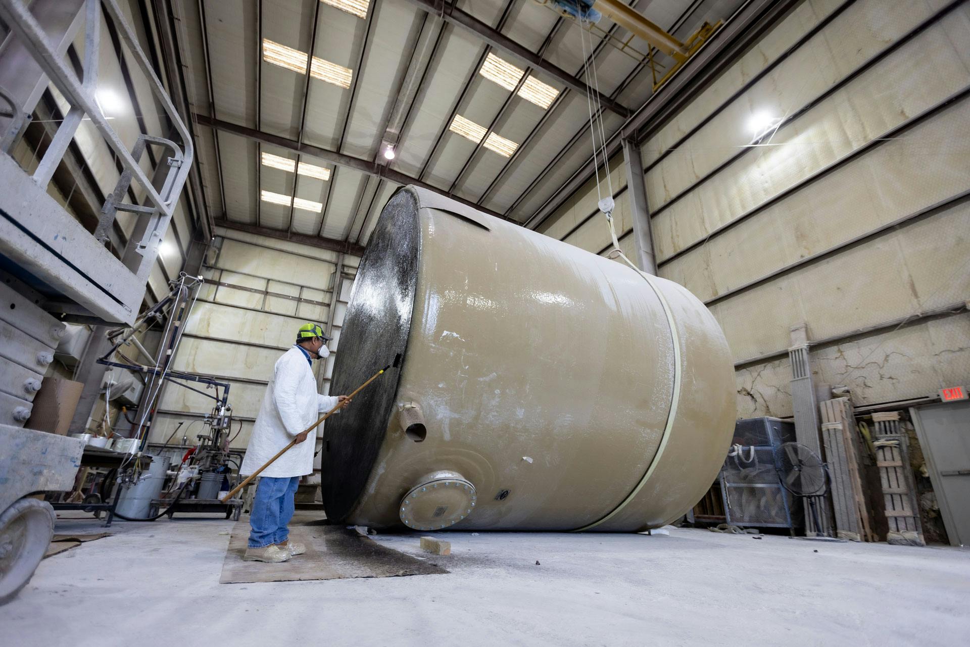 Fiberglass tank laying on its side. Factory worker applying coating to bottom with brush. 