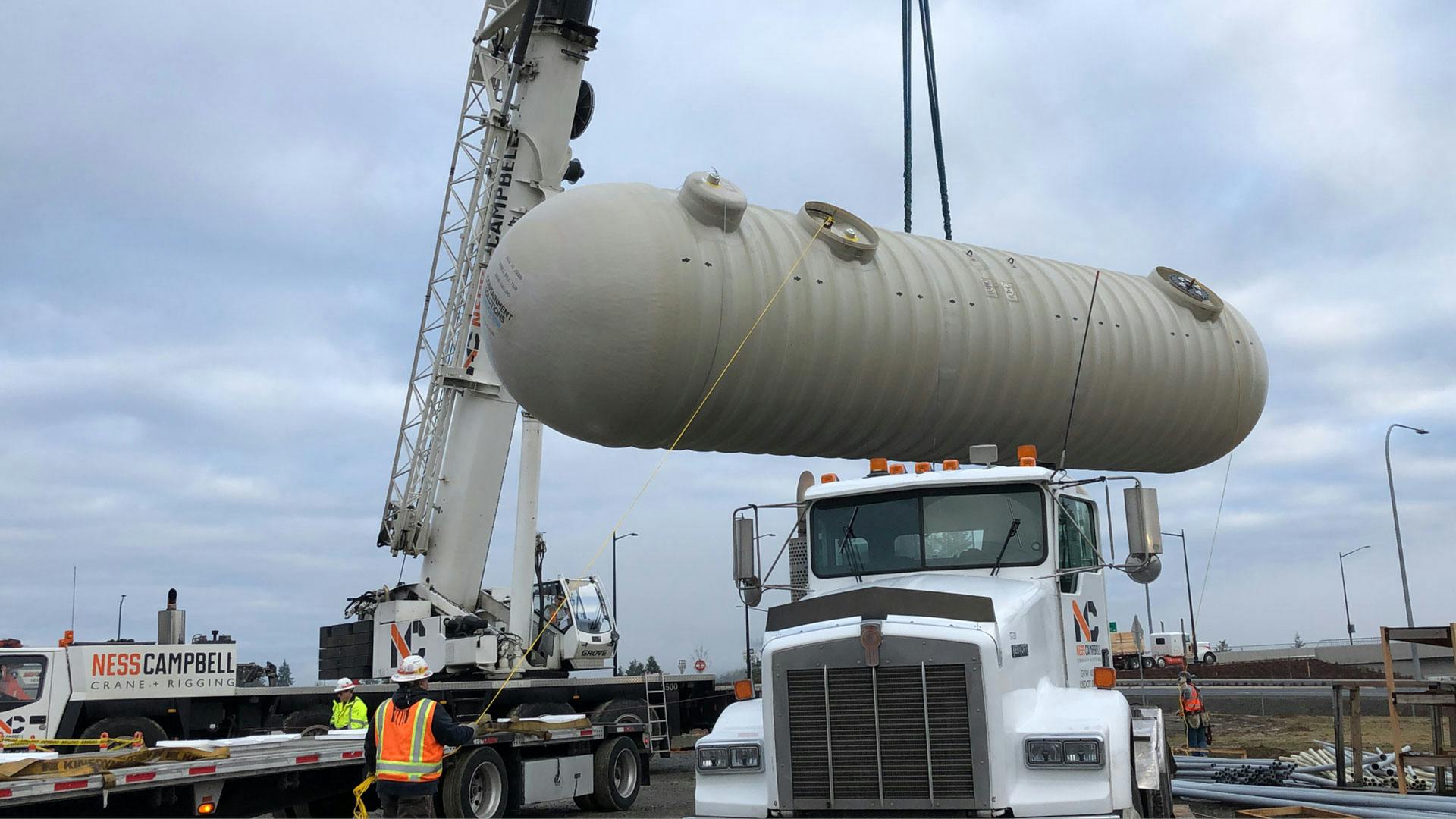 Fiberglass tank being lifted off delivery truck with a crane. 