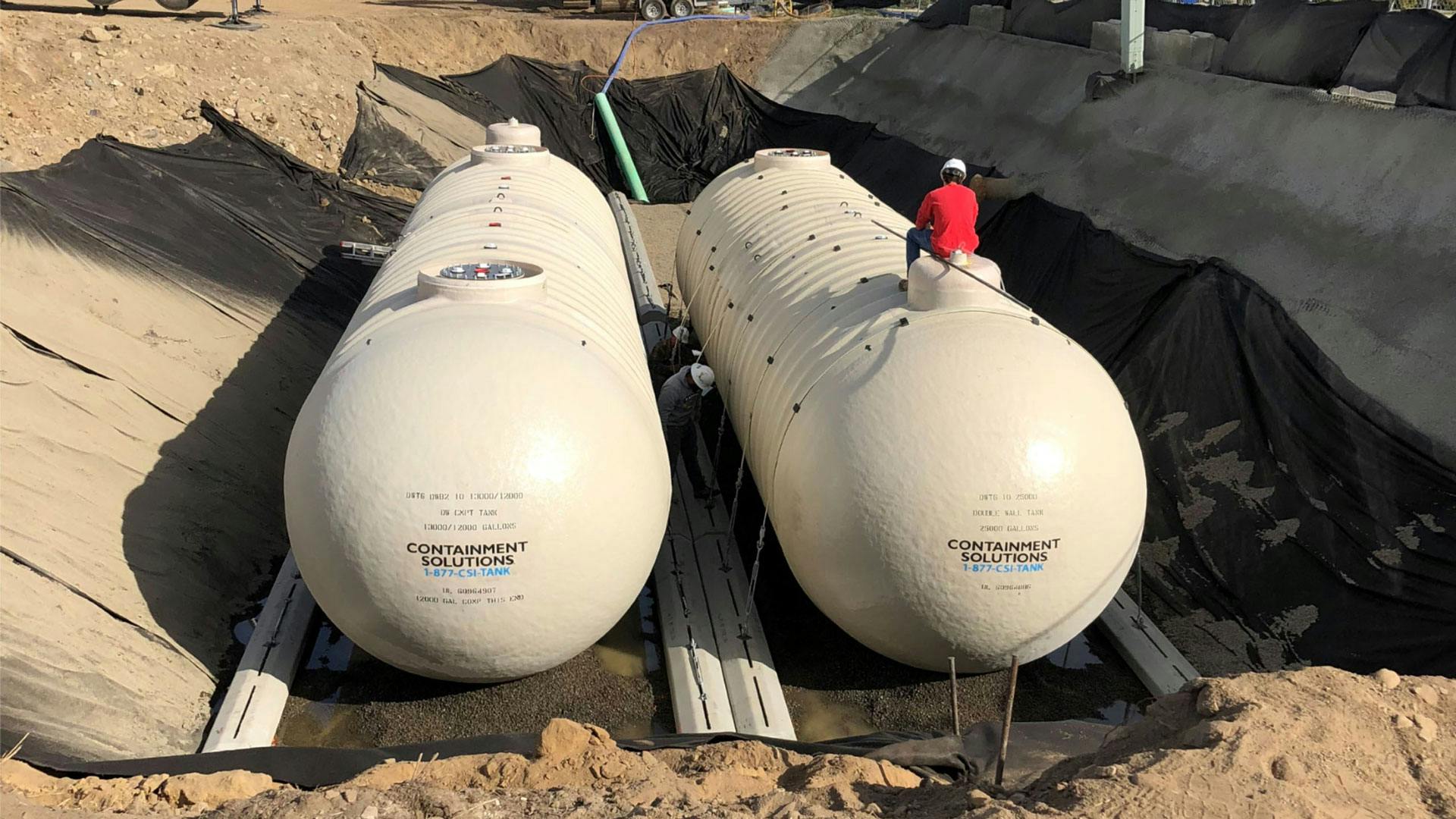 Two fiberglass tanks on job site with worker on top of tank.