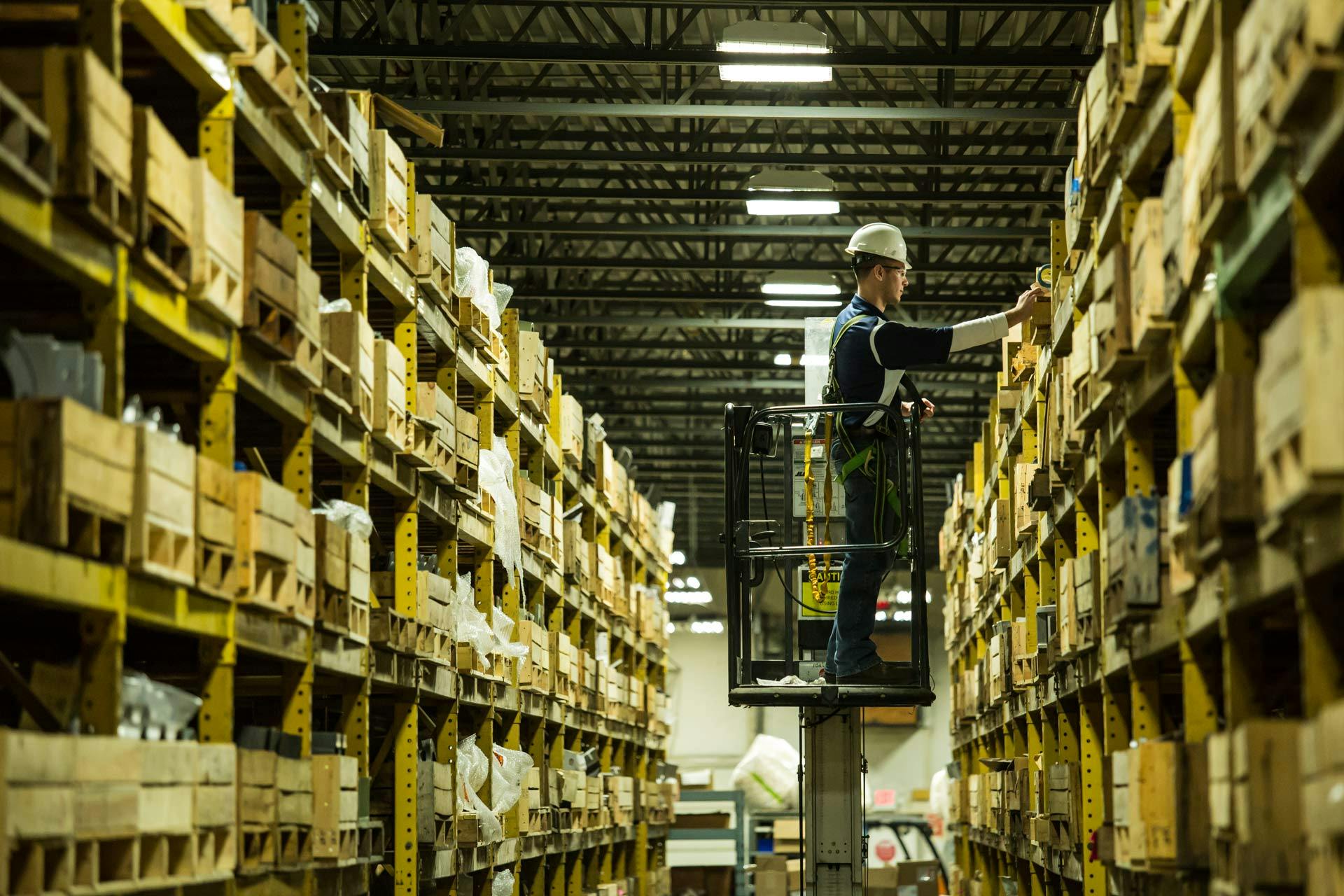 Man on lift in front of stock shelves in spare parts facility