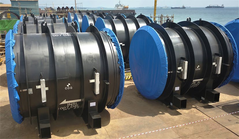 Image of rows of balck, large diameter pipes and cylindrical products with blue plastic coverings at the ends