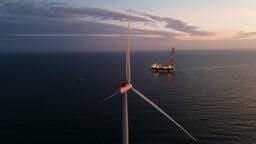 Offshore wind turbine and support vessel at dusk.