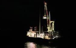 Brightly lit construction rig with crane on water at night.