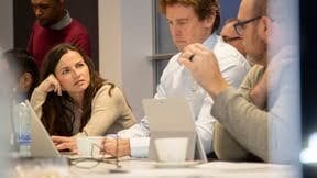 Woman focused on laptop during a meeting with colleagues.