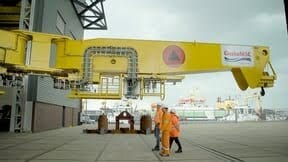 Large yellow industrial arm with workers in safety gear and a ship in a port.