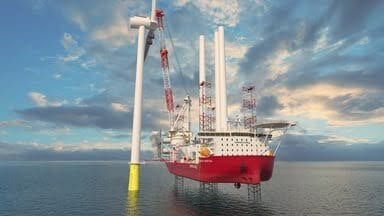 Red jack-up vessel installing white offshore wind turbine at sea.
