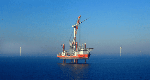 Offshore platform installing a wind turbine in a wind farm at sea under a blue sky.