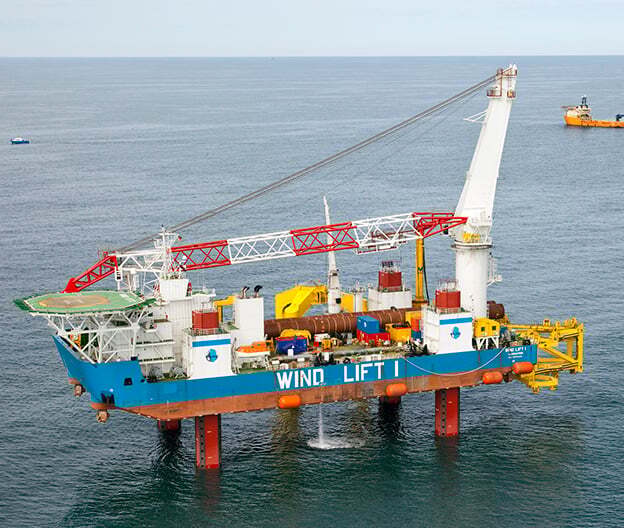 Offshore jack-up vessel "WIND LIFT I" with a large crane and helipad, extending legs into the sea.