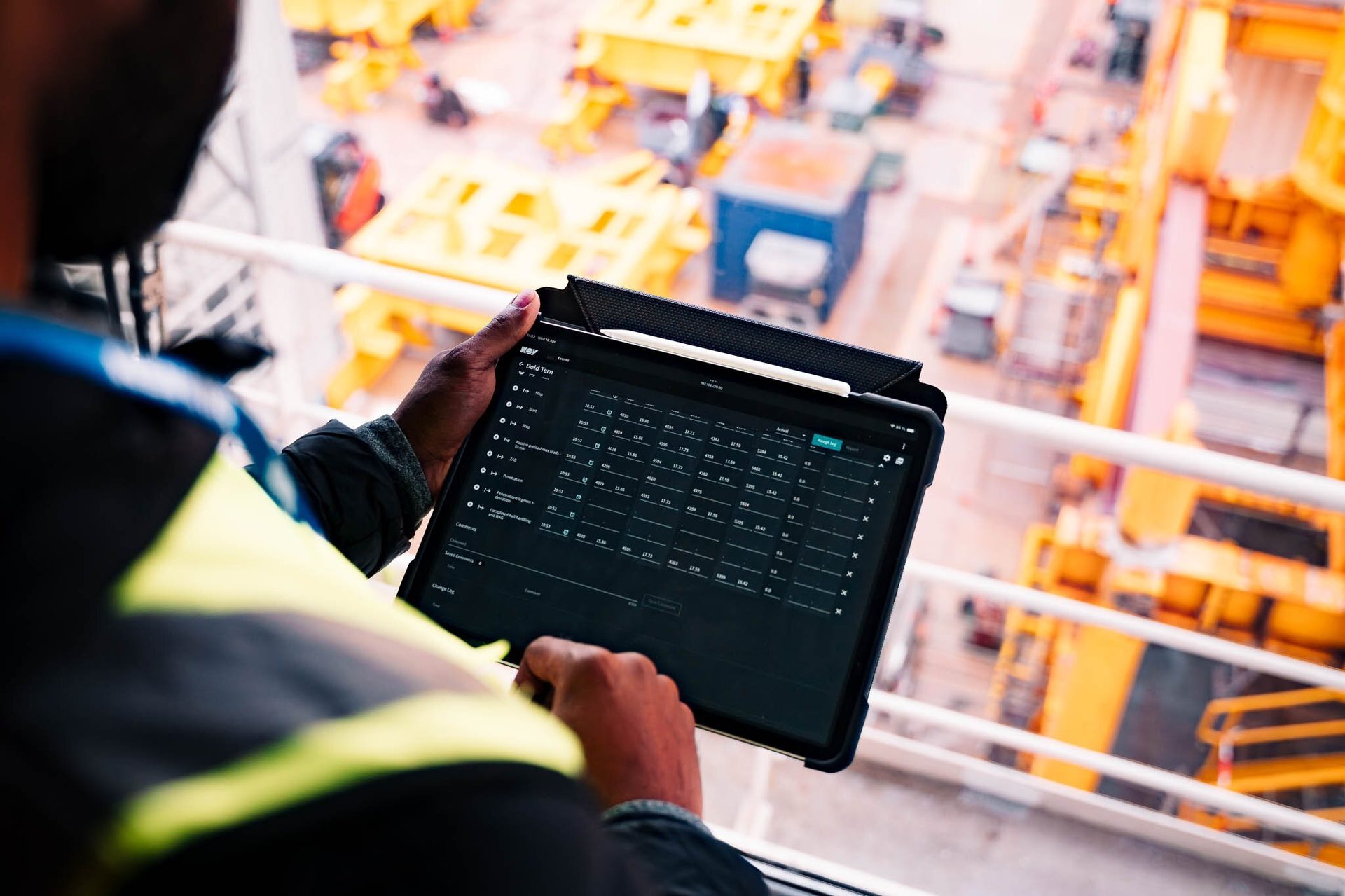 Worker in high-vis vest viewing a data log on a tablet, overlooking a construction site.