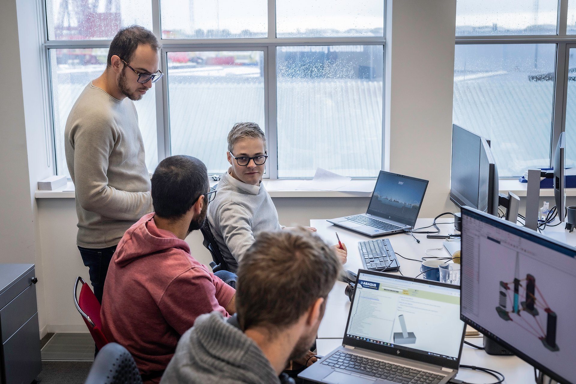 Four men collaborating on computers in a bright office.