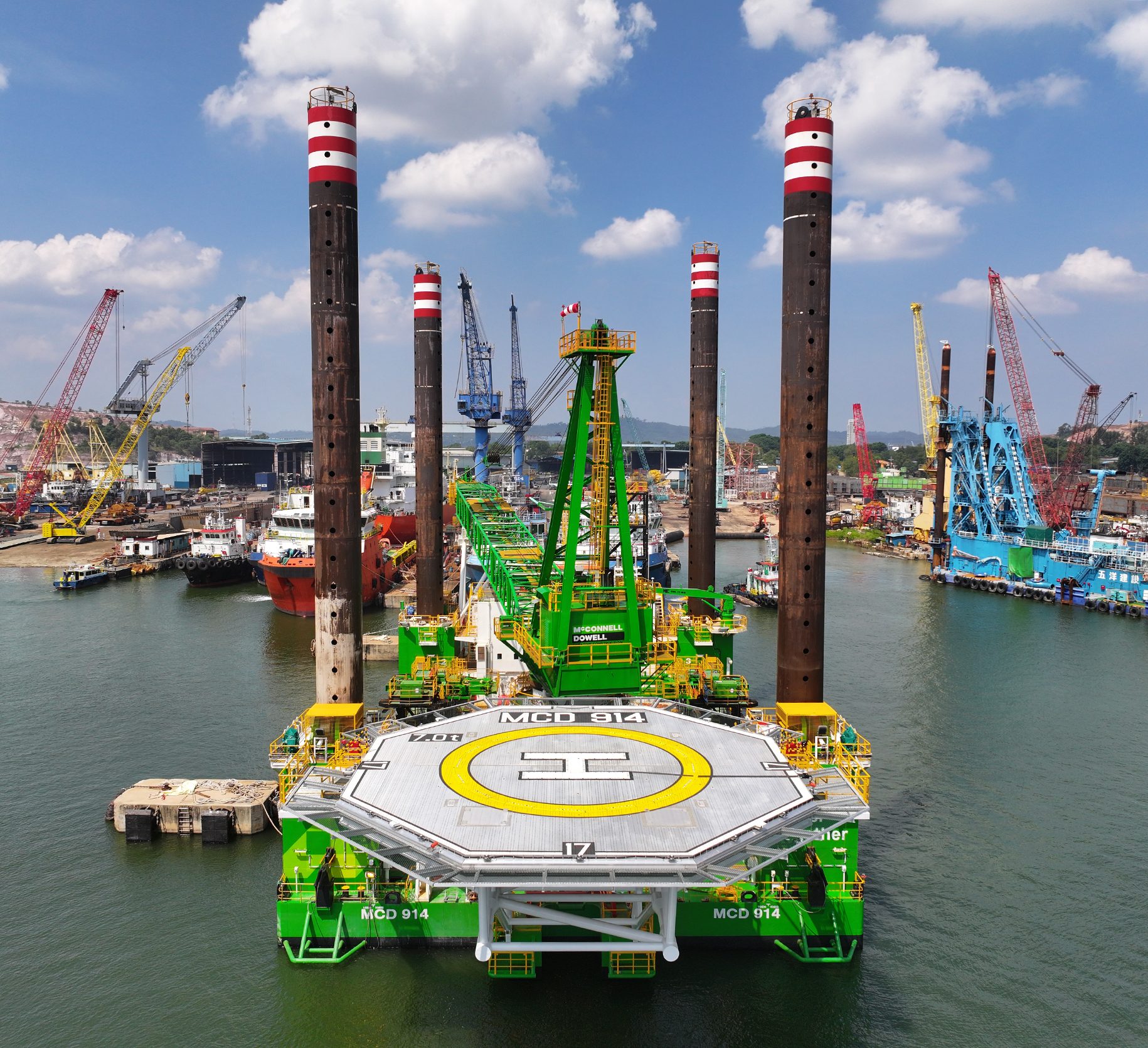 Green jack-up vessel with four tall legs and new helicopter platform at port