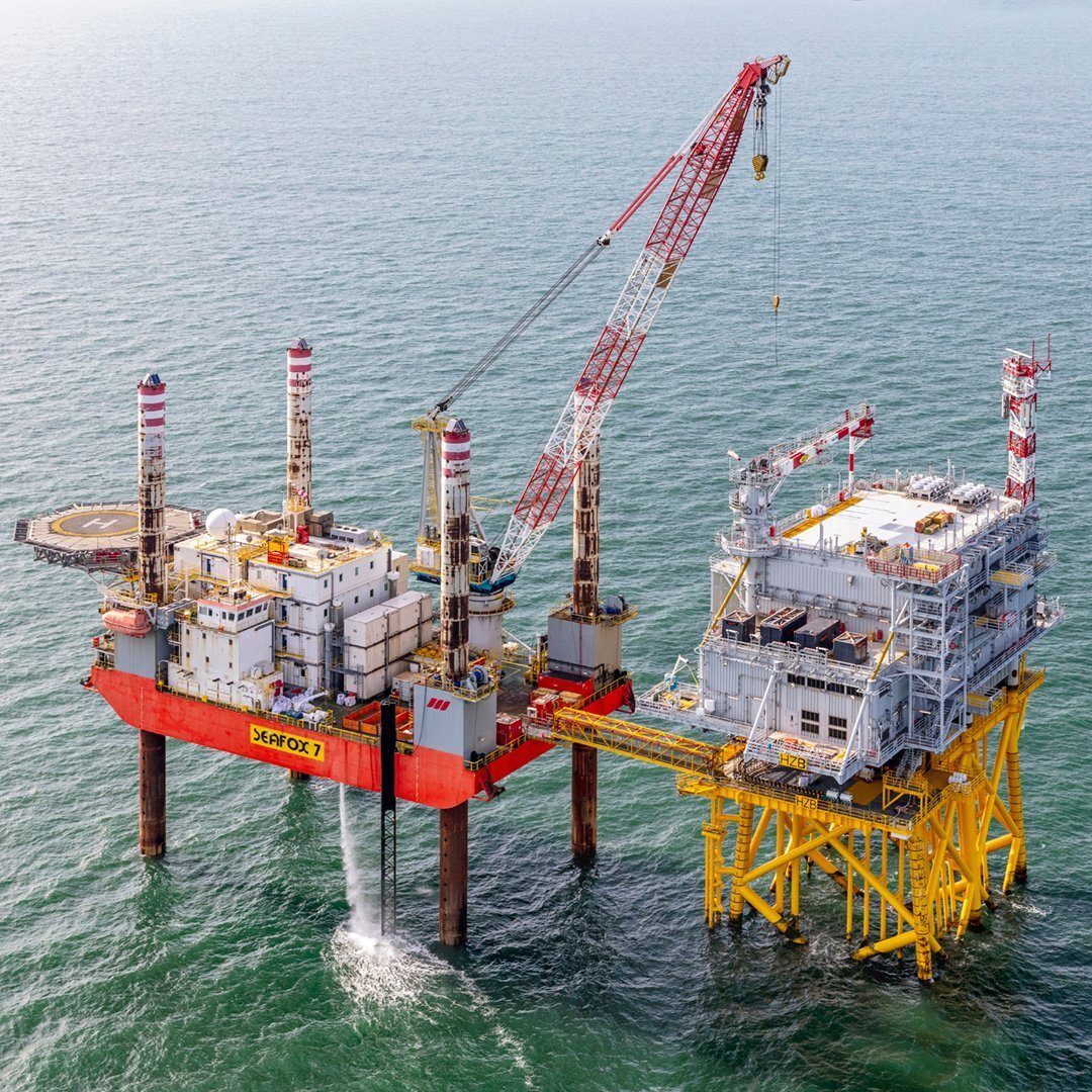 Red 'SEAFOX 7' offshore jack-up rig with large crane, connected to a yellow platform in the sea.